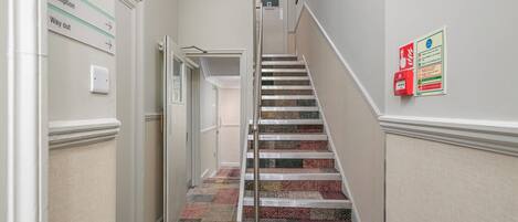 A hallway with a carpeted staircase, a reception sign, and a fire safety sign.