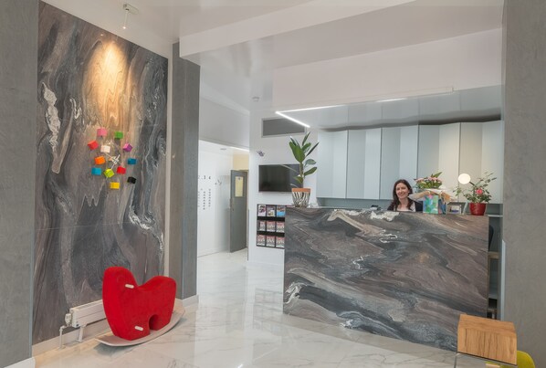 Welcome to our reception area, featuring a stylish desk and vibrant artwork, complemented by lush greenery and a unique chair.