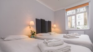 A hotel room with two beds, white linens, a window with blinds, and wall-mounted lamps. - Victoria Inn (London)