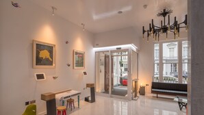 A modern lobby with a glass door entrance, a green chair, a red chair, a black bench, and a chandelier. - Victoria Inn (London)