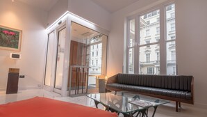 A modern living room with a glass coffee table, a leather sofa, and a large window offering a view of buildings. - Victoria Inn (London)