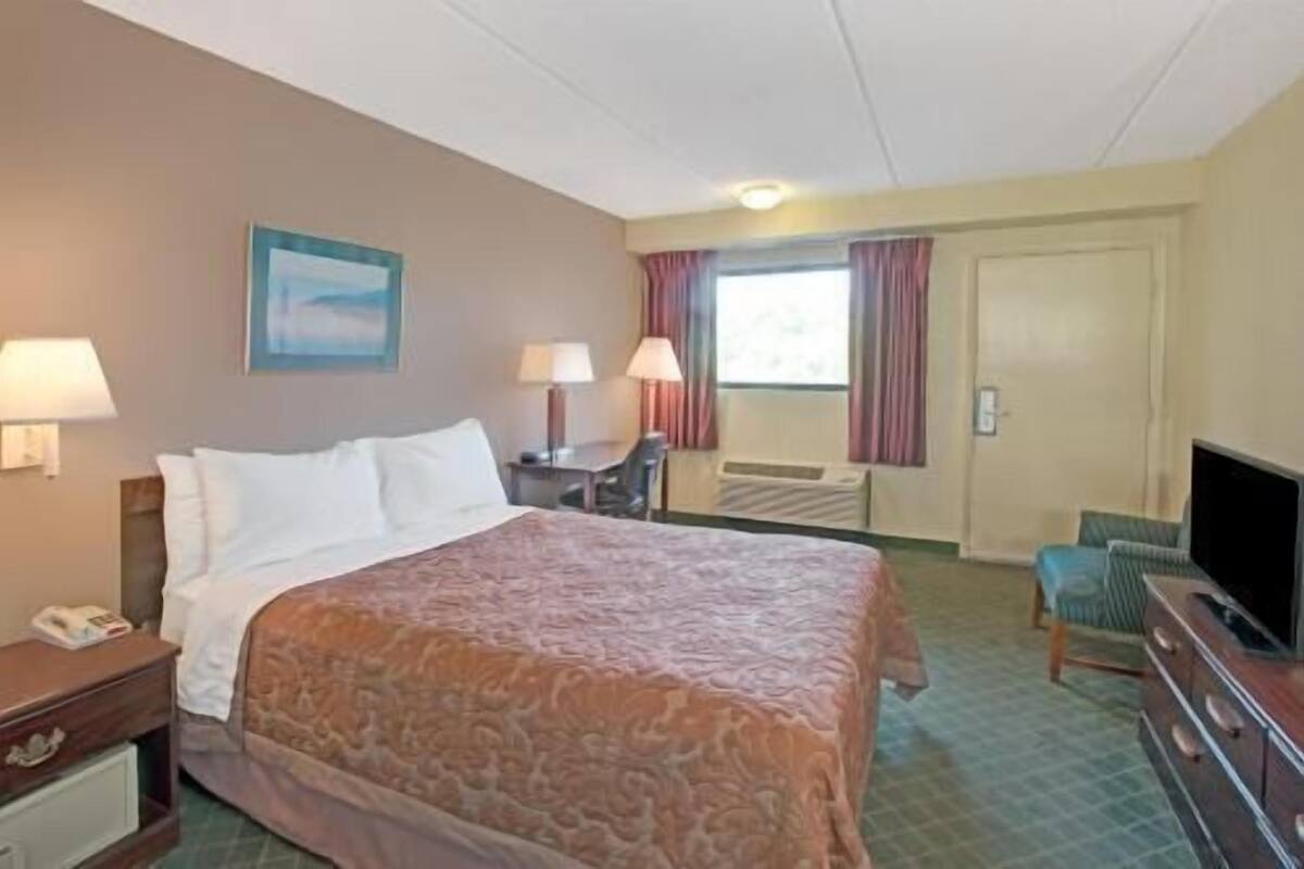 A hotel room with a bed, two bedside lamps, a desk, a chair, a television, and a window with curtains.