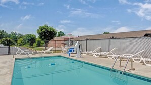 A rectangular swimming pool with a tiled edge, surrounded by white lounge chairs and a fence. - Super 8 by Wyndham Shelby (Shelby)