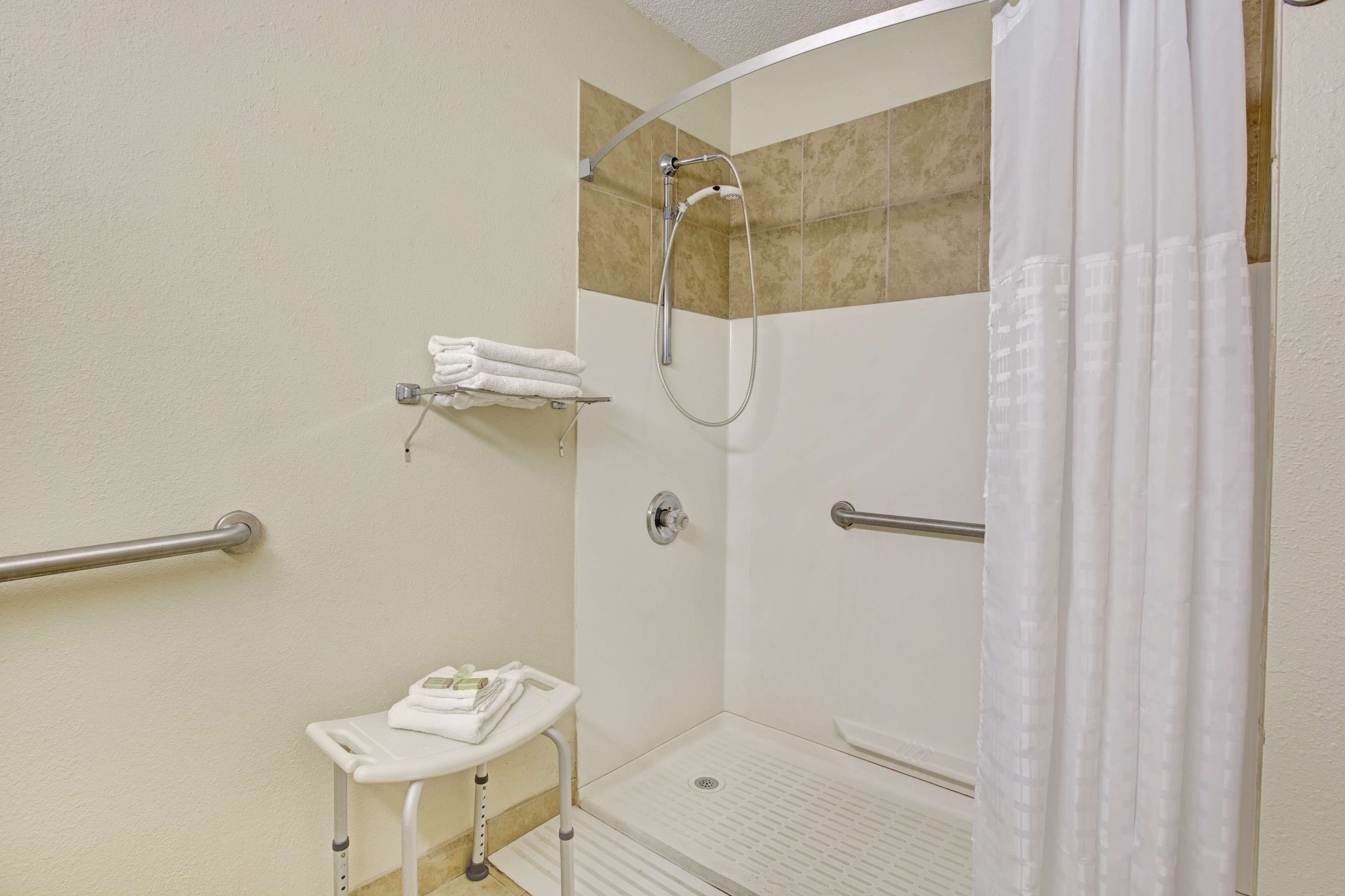 Area doccia accessibile con barra di sostegno, porta asciugamani bianco e pannello comandi.