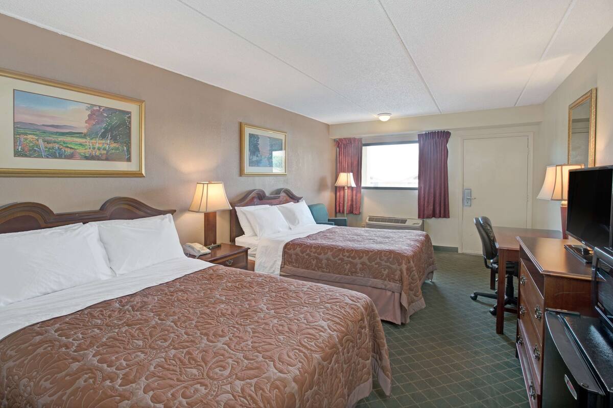 A hotel room with two beds, a desk, a chair, a television, and a window with curtains.