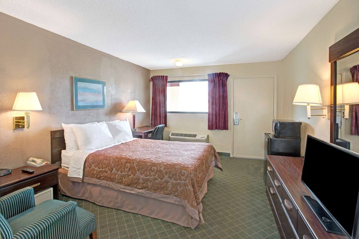A hotel room with a bed, a desk, a chair, a TV, and a mirror.