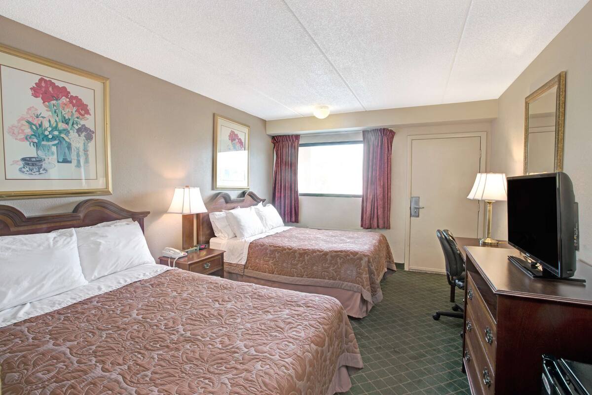 A hotel room with two beds, a desk with a TV, a dresser, and a window with curtains.