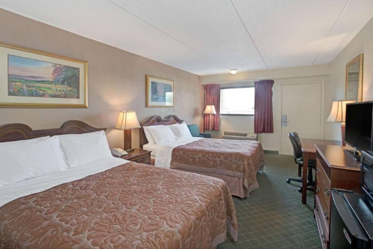 A hotel room with two beds, a desk, a chair, a television, and a window with curtains.