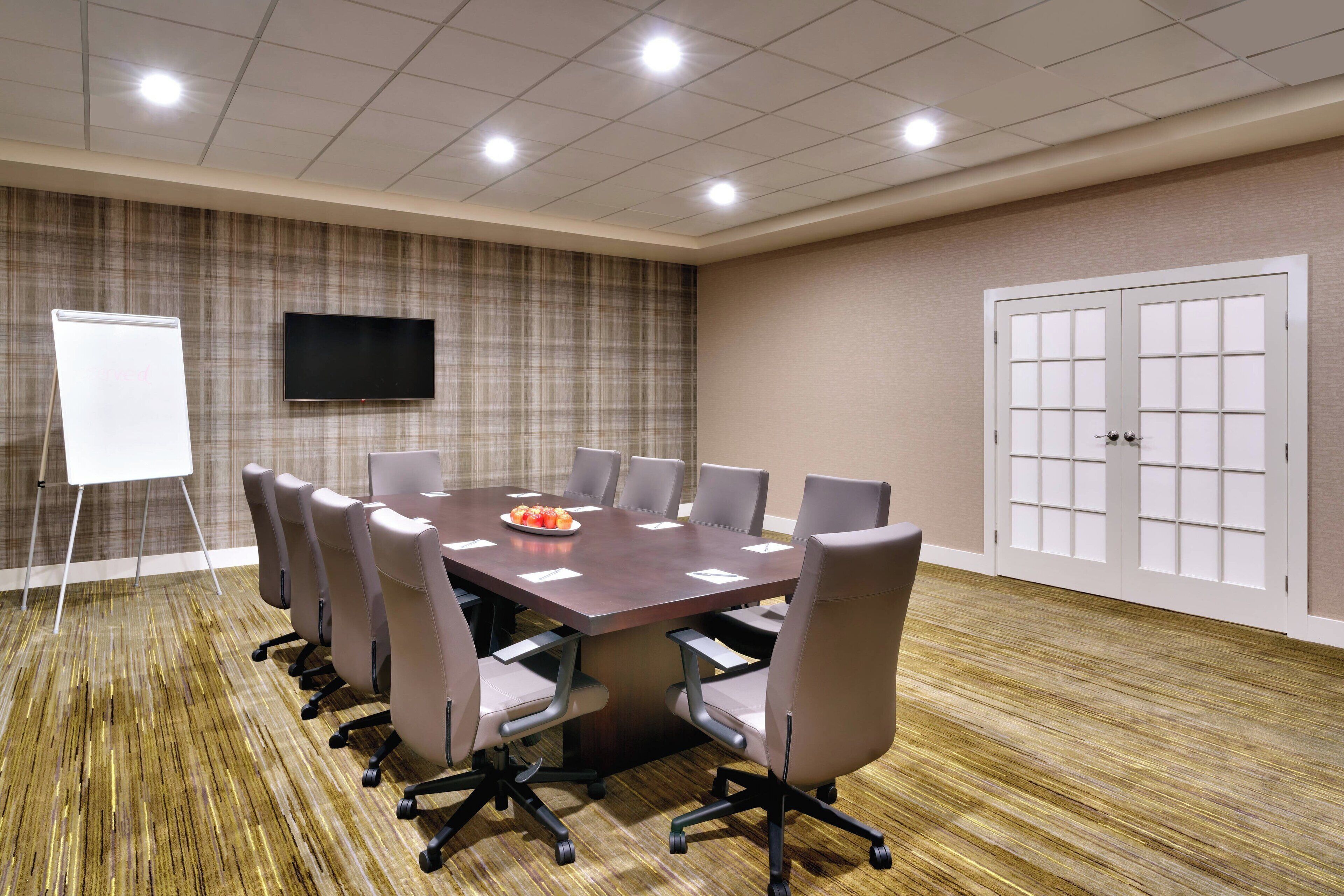 A conference room with a large table, chairs, a whiteboard, a TV, and a door.