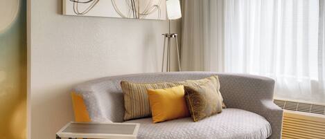 A modern living room with a grey sofa, a small side table, a floor lamp, and a large abstract painting on the wall.