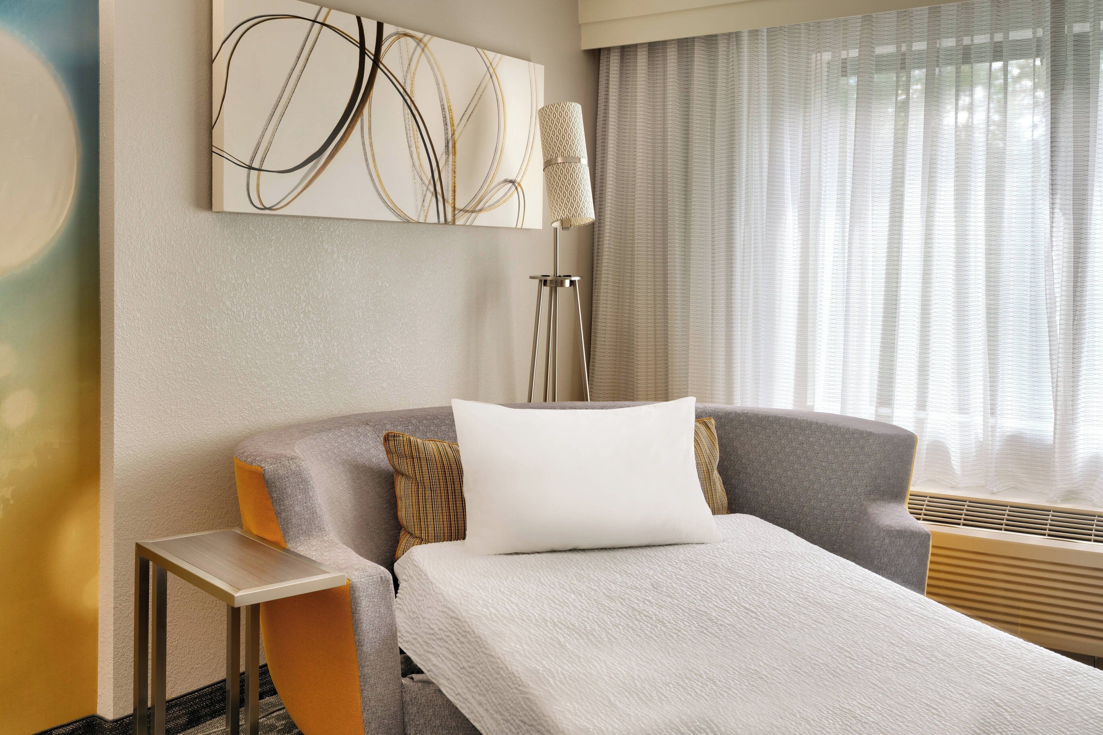 Una habitación de hotel moderna con una cama, una lámpara de pie y un cuadro abstracto grande en la pared.