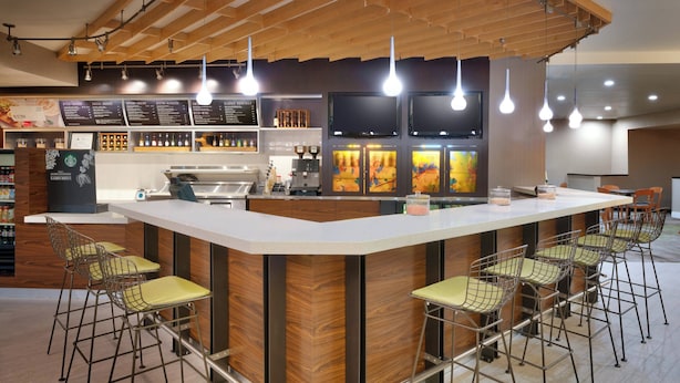 Un área de bar moderna con techo de madera, lámparas colgantes, una barra central y taburetes con asientos acolchados.