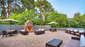 Un patio al aire libre con suelo de ladrillo, chimenea de piedra y mobiliario exterior.