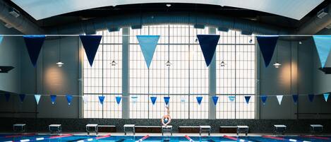 An indoor swimming pool with lanes, benches, and a large window with blue triangular flags.