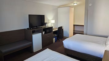 A hotel room with two beds, a desk with a television, a small refrigerator, and a chair.