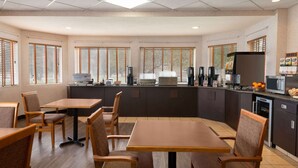 A modern restaurant with wooden tables and chairs, a kitchen area with appliances, and large windows with blinds. - Days Inn by Wyndham Swift Current (Swift Current)