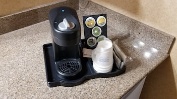 Een koffiezetapparaat met een lekbak, een flesje room en een suikerpotje op een granieten aanrecht.