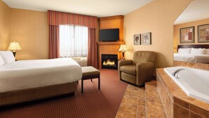 A hotel room with a large bed, a chair, a fireplace, a TV, and a bathroom with a bathtub. - Days Inn by Wyndham Swift Current (Swift Current)