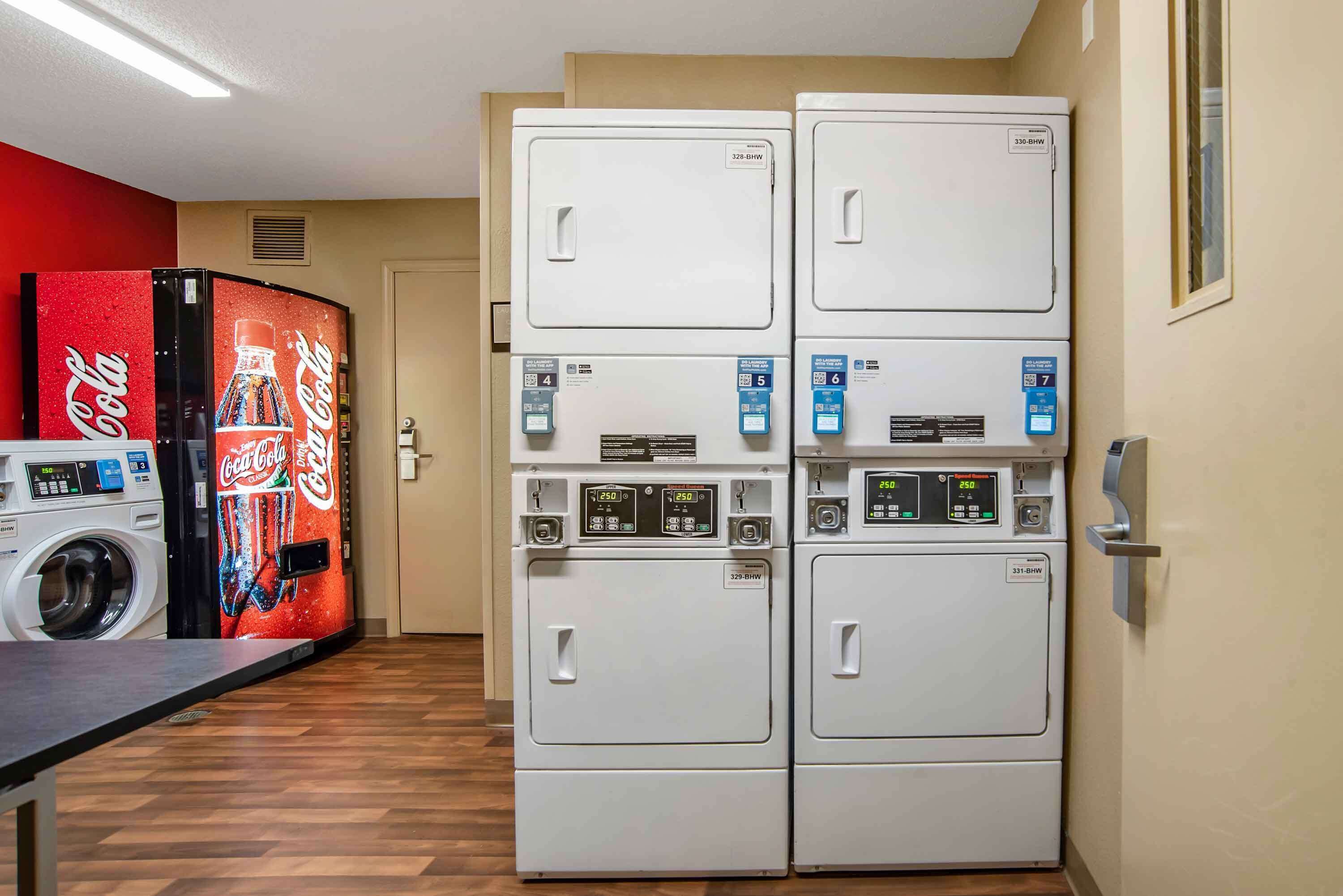 Un espace buanderie équipé de deux machines à laver, d’un sèche-linge et d’un distributeur automatique de Coca-Cola.