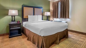 A hotel room with a bed, two bedside tables with lamps, a nightstand, a window with curtains, and a green wall.