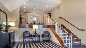 A spacious living area with a striped carpet, a staircase with wooden railings, and two leather chairs.