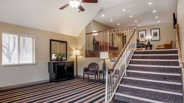 A spacious living room with a large window, a staircase with a railing, and a dark wood floor.