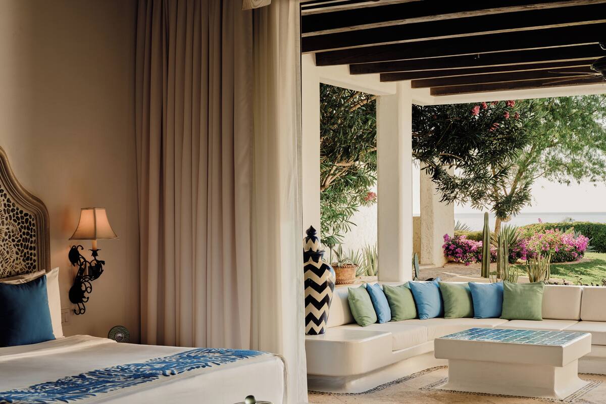 A bedroom with a bed, a nightstand, a lamp, a sofa, and a view of the outdoors.
