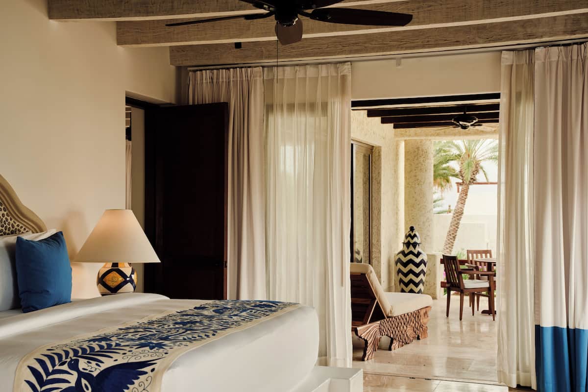 A hotel room with a bed, a lamp, a view of a pool area, and a ceiling fan.