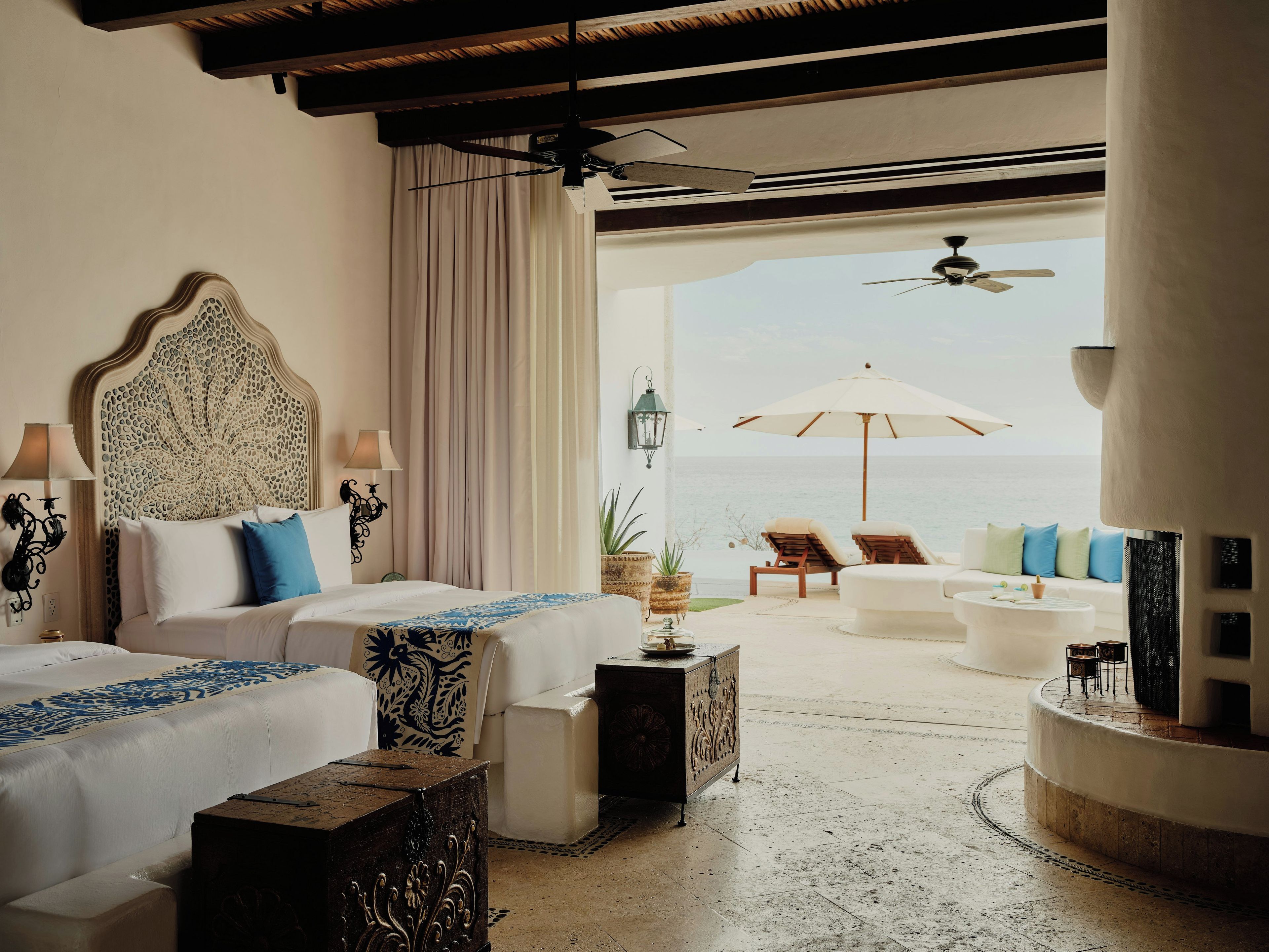 A hotel room with two beds, a view of the sea, and a balcony with seating.