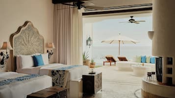 A hotel room with two beds, a view of the sea, and a balcony with seating.