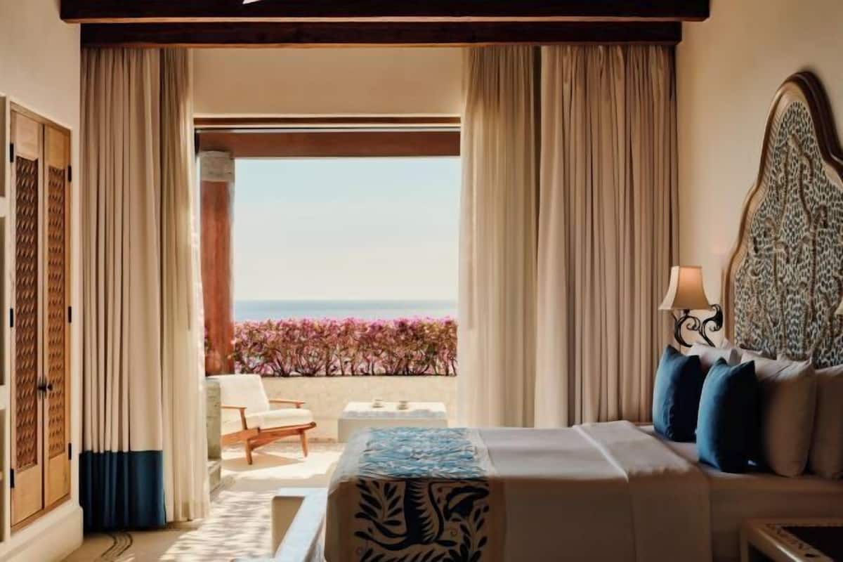 A hotel room with a bed, a nightstand, a lamp, and a view of the ocean.