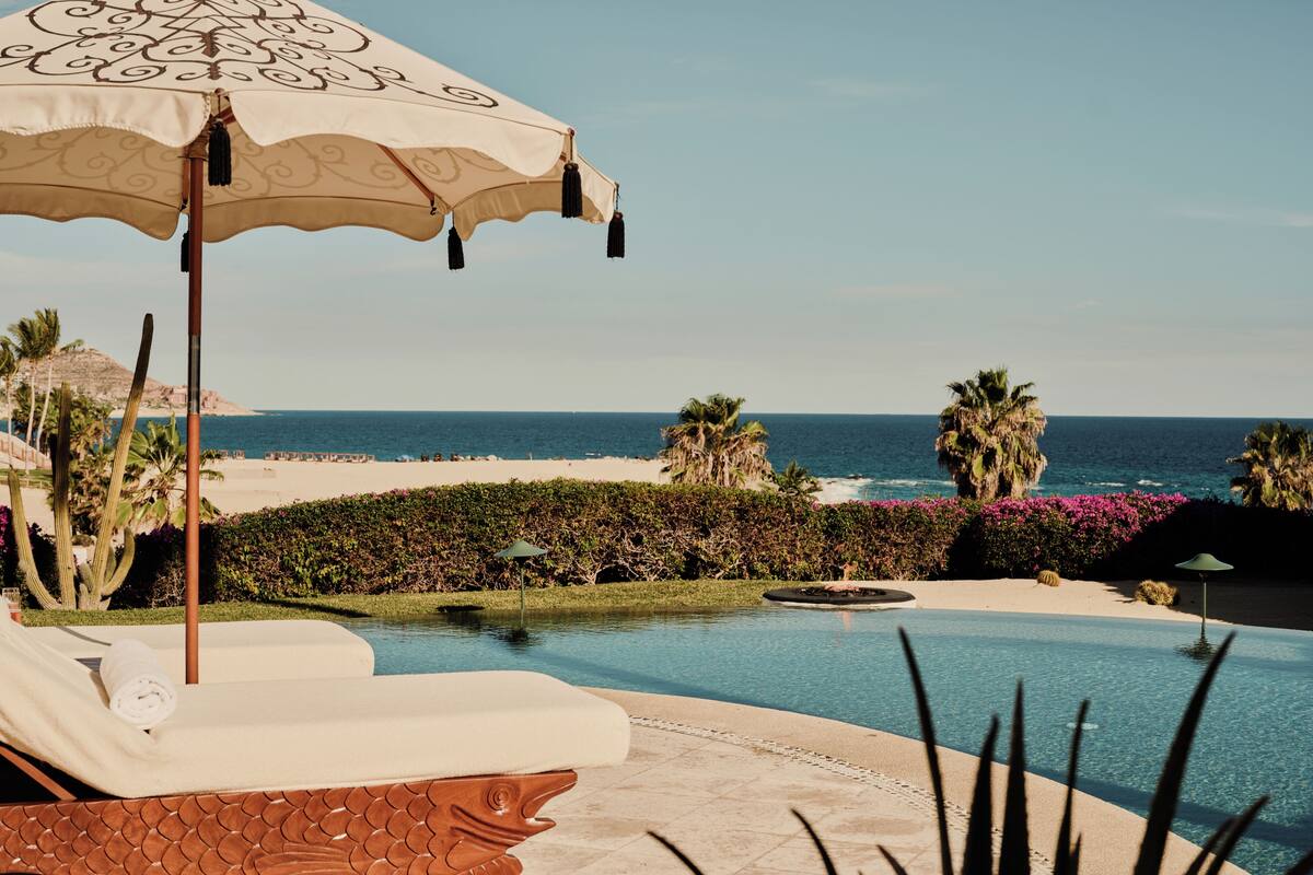 A pool with a wooden fish-shaped edge, a lounge chair, and an umbrella.