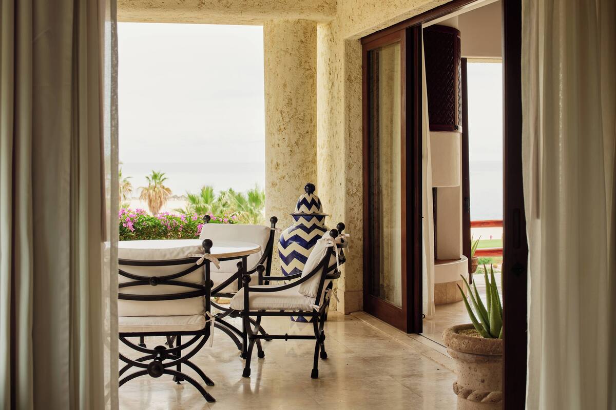 A balcony with a view of the ocean, a table with chairs, and a potted plant.