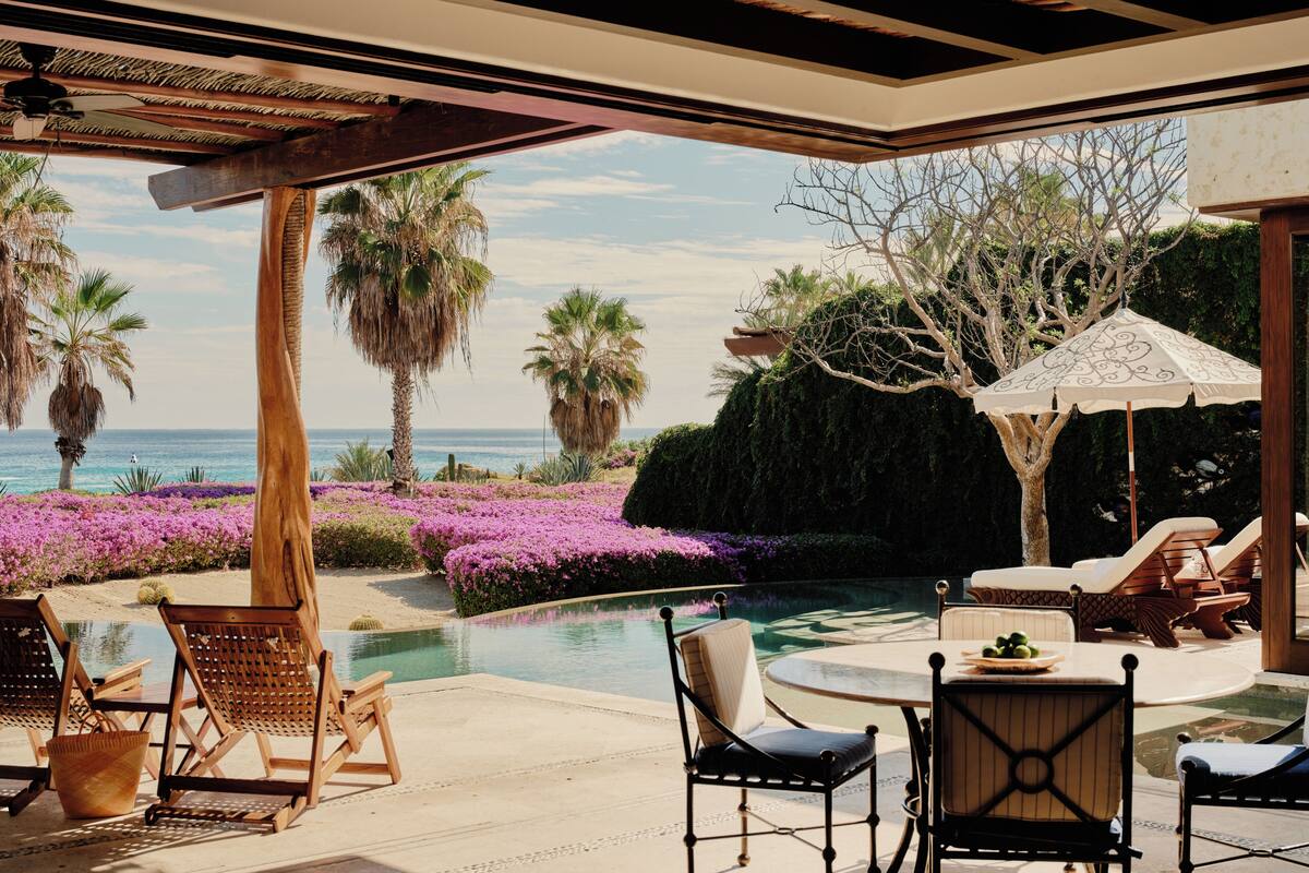 A poolside area with lounge chairs, a table, and a view of the ocean.
