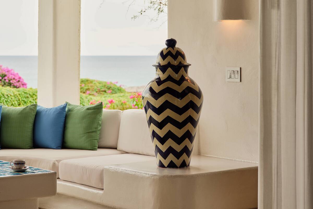 A room with a white sofa, a patterned vase, and a view of the sea.