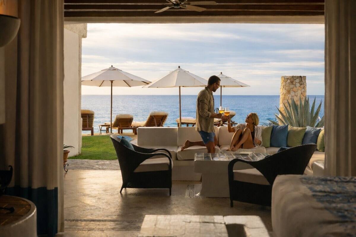 A hotel room with a view of the ocean, a balcony with outdoor seating, and a stone pillar.