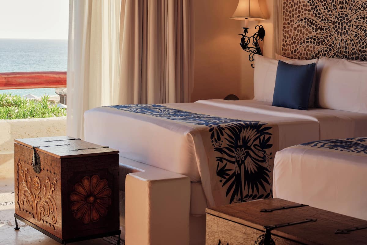 A hotel room with a large bed, a bedside table, a decorative headboard, and a view of the ocean.