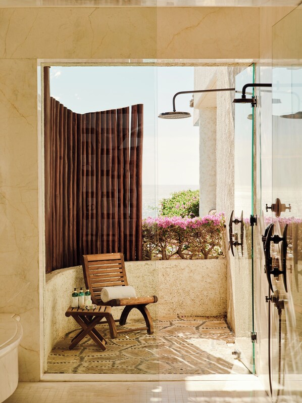 Une salle de bain avec une douche, une chaise en bois et une petite table avec des articles de toilette.