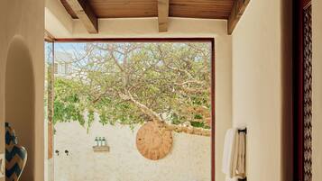 A bathroom with a bathtub, a towel rack, and a view of a tree and wall outside.