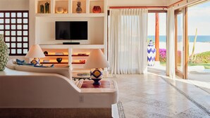 A modern living room with a flat-screen TV, wooden beams, a sofa, and a view of the ocean.