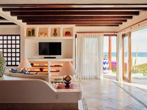 A modern living room with a flat-screen TV, wooden beams, a sofa, and a view of the ocean.
