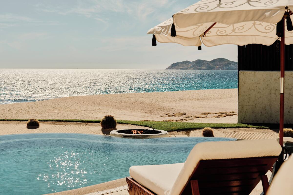 A pool with a view of the ocean, a lounge chair, and a decorative umbrella.