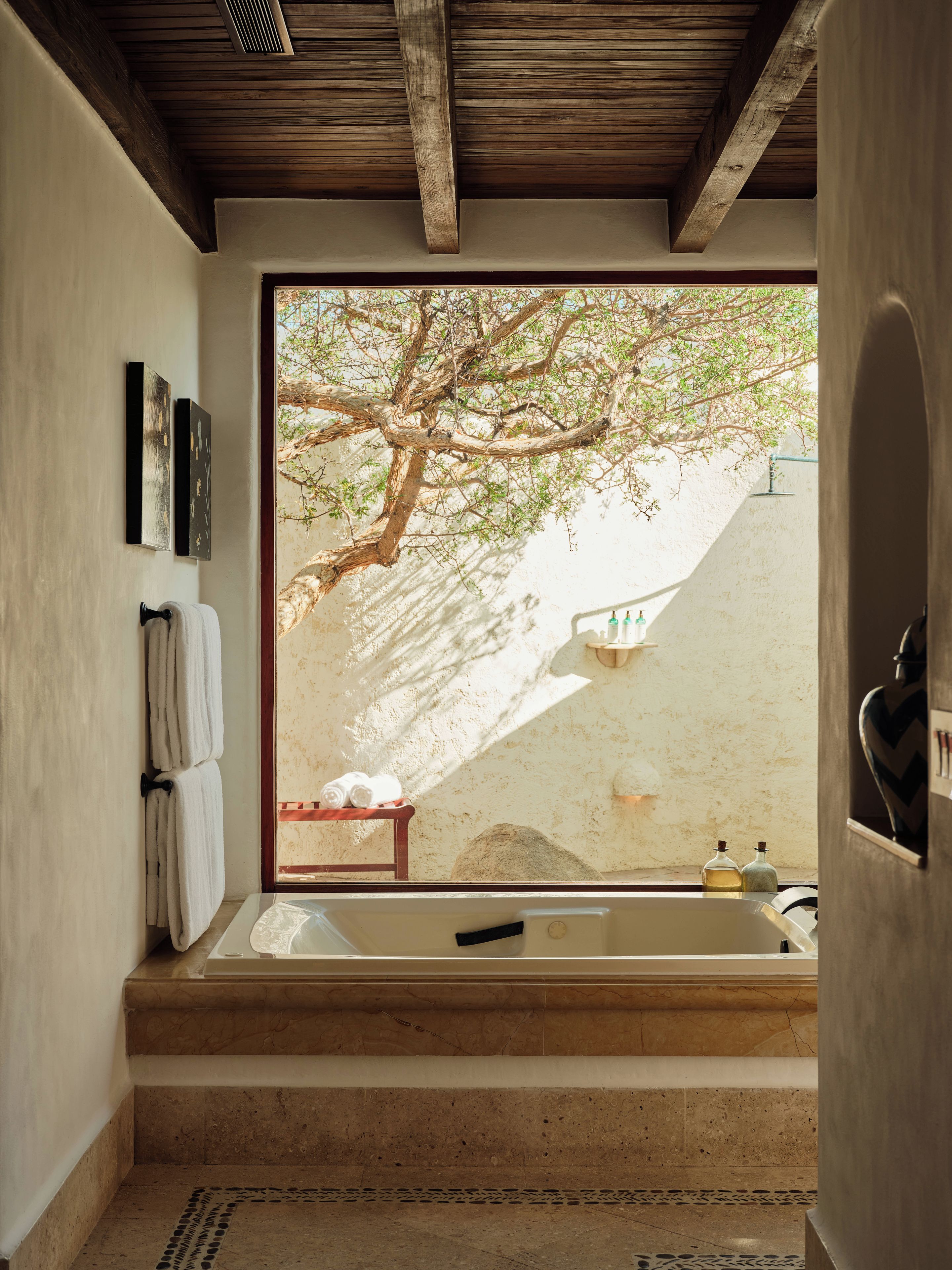 A bathroom with a bathtub, a towel rack, and a view of a tree outside.