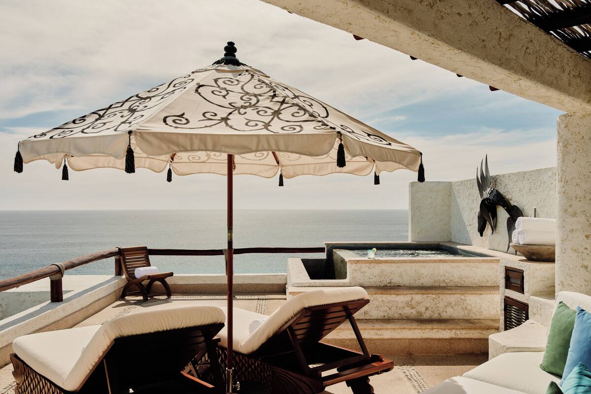 An outdoor seating area with a patterned umbrella, lounge chairs, and a view of the sea.