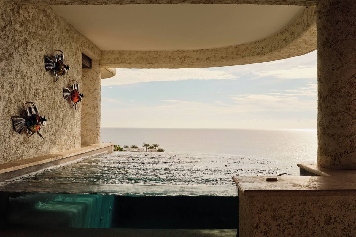 A room with a view of the sea, a bathtub, and three decorative fish.