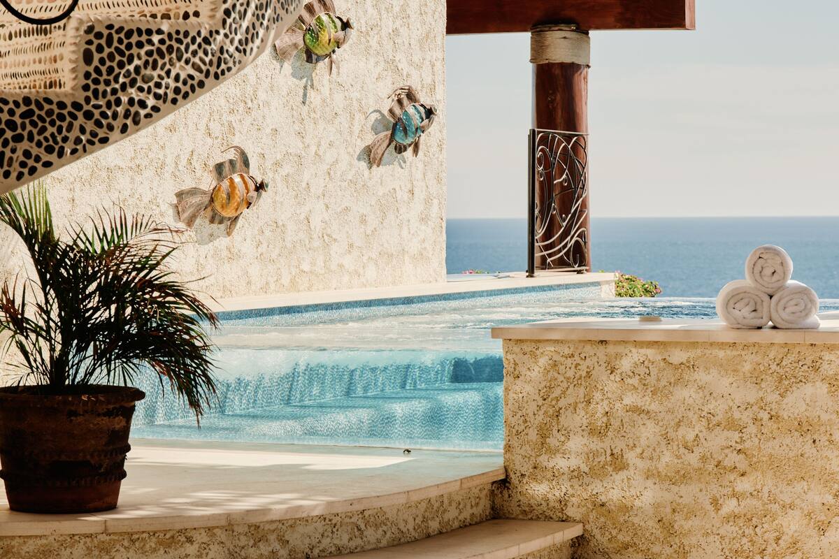 A poolside area with a view of the ocean, a pergola, and a seating area with towels.