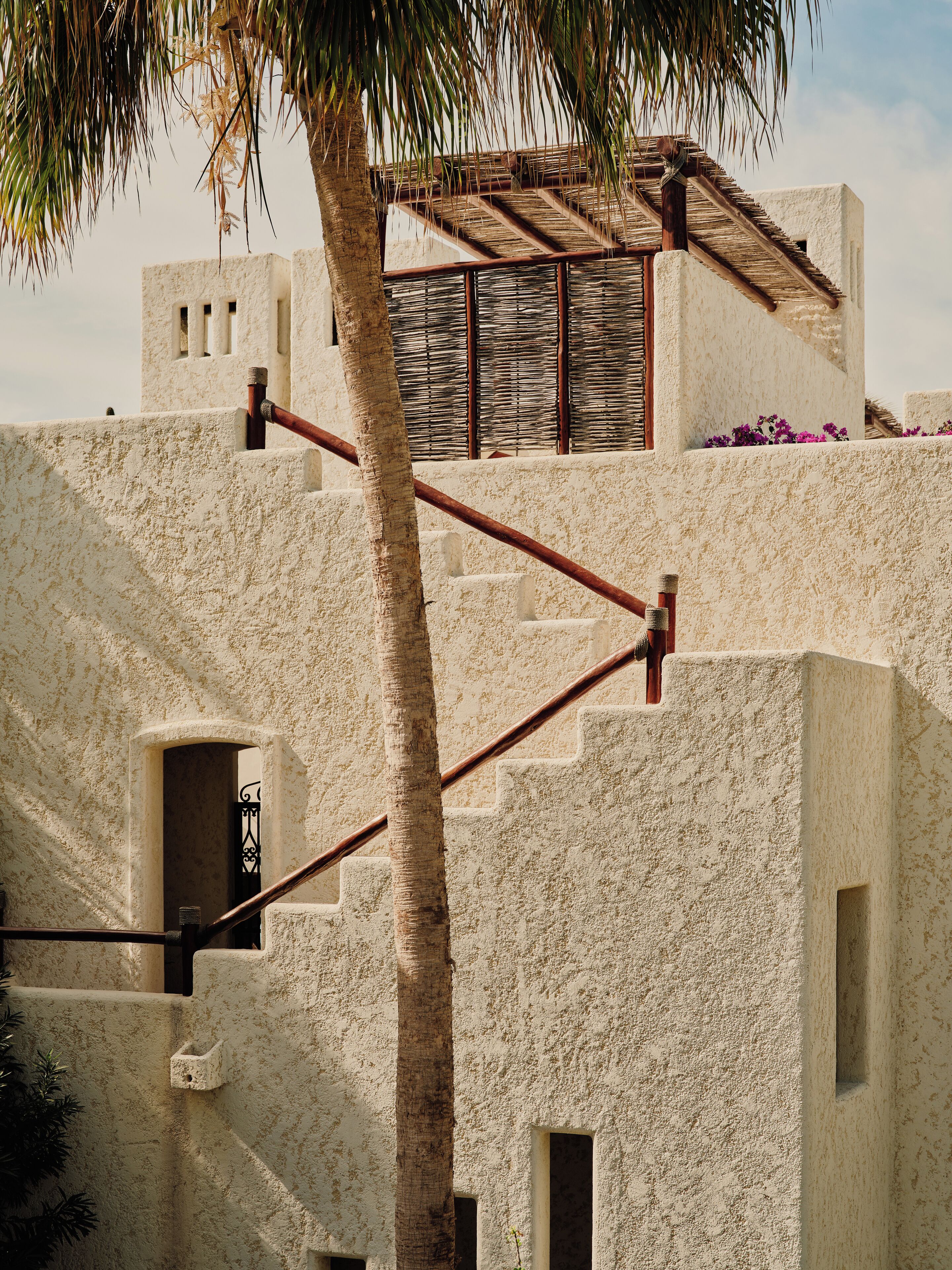 A building with a textured facade, a palm tree, and a staircase leading to an upper level.