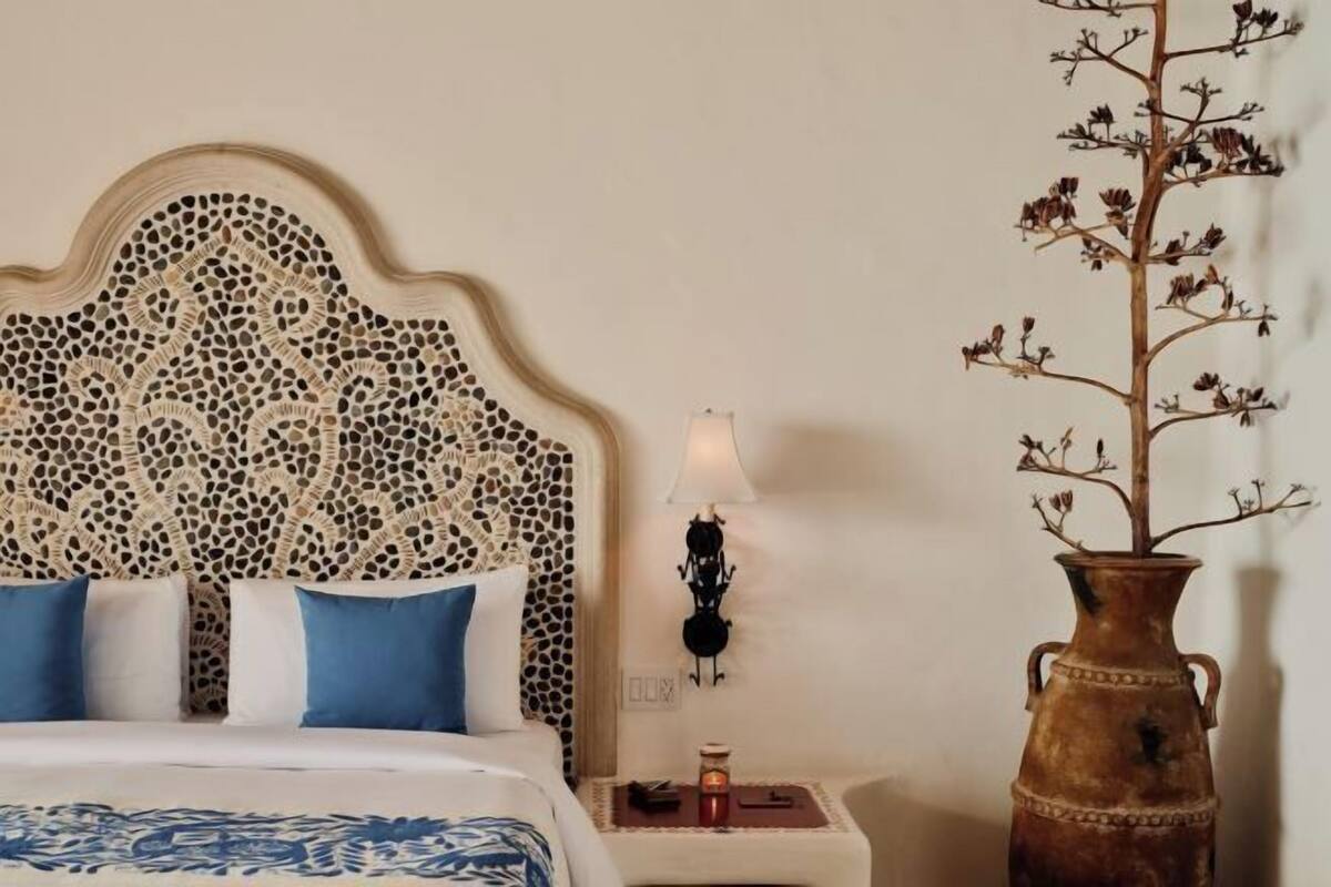 A bed with a decorative headboard, a bedside table with a lamp, and a vase with dried flowers.