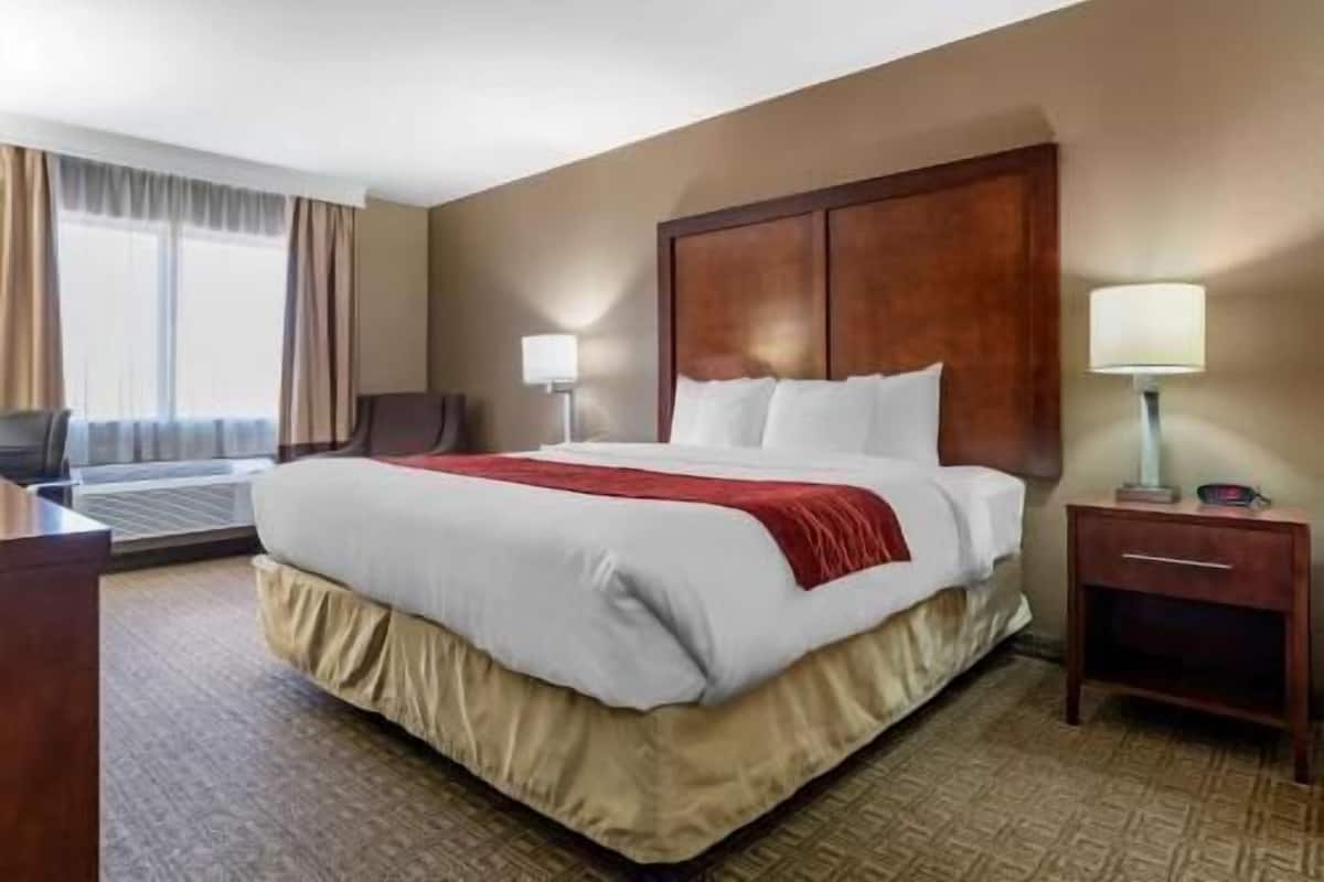 A hotel room with a large bed, two bedside lamps, a wooden headboard, a desk, and a chair.