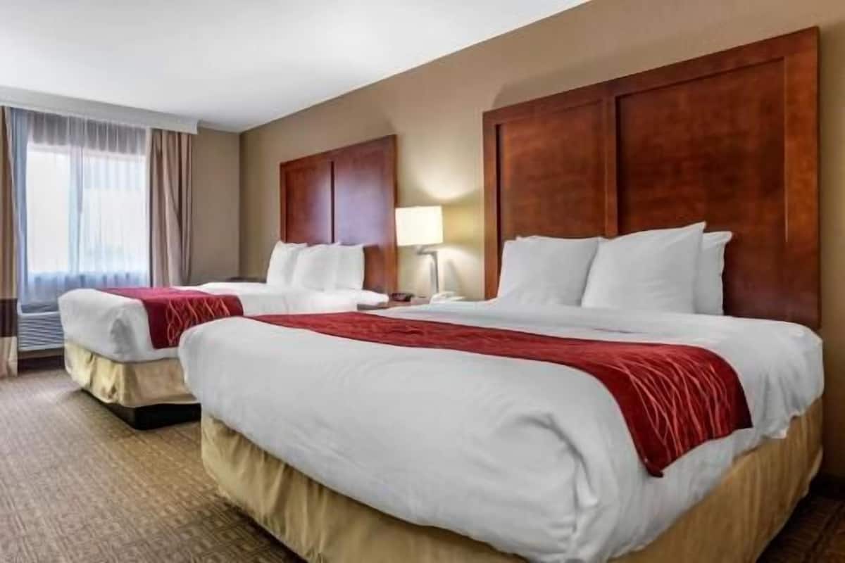 A hotel room with two beds, a wooden headboard, a lamp, and a window with curtains.
